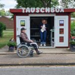 Mann mit Rollstuhl und Frau stehend in bzw. vor der Tauschbox