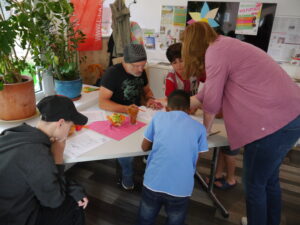 3 Kinder und 2 Erwachsene um einen Tisch beim Bearbeiten von Lernmaterial